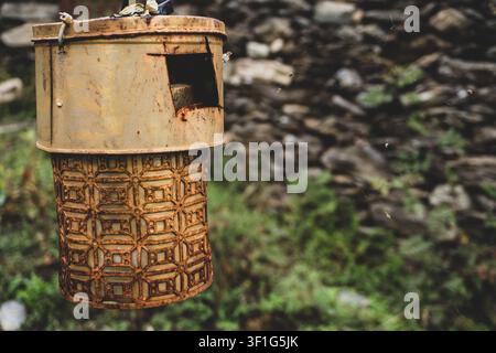 Rusty hanging metal lantern with a patterned lower section against a blurred outdoor stone and greenery background. Uttarakhand India Stock Photo