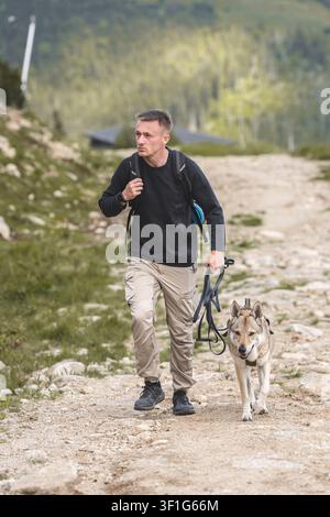 Man with backpack walking dog on leash along rocky mountain dirt trail, outdoor hiking with pet and active lifestyle concept. . High quality photo Stock Photo