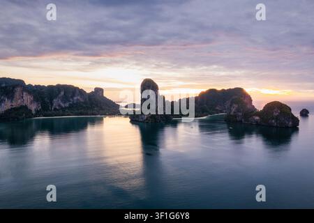 Aerial view of Railay Beach with dramatic limestone cliffs rising from the calm sea under a soft sunset sky in Ao Nang, Krabi, Thailand. Stock Photo