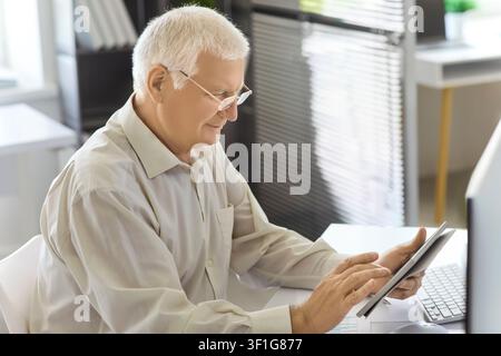 Senior man using tablet at office desk, analyzing data and managing finances Stock Photo