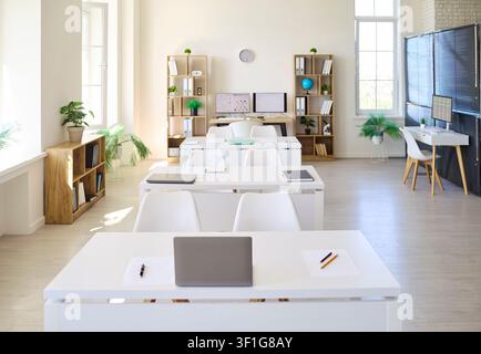 Front view of bright modern classroom with white desks, laptops and bookshelves Stock Photo