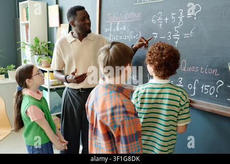 Black Male Teacher Guiding Children Solving Math Problems in Class Stock Photo