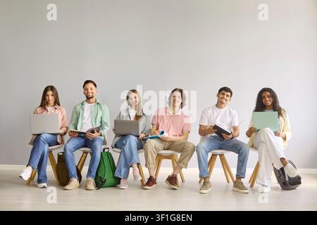 Happy students with laptops in classroom against gray background, teamwork Stock Photo