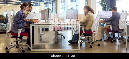 Finance team working on reports at computers in modern open plan office workspace Stock Photo