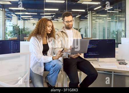 Coworkers collaborating on laptop in modern office, reviewing code and insights Stock Photo