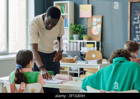 Black Male Teacher Assisting Students during Classroom Lesson Stock Photo