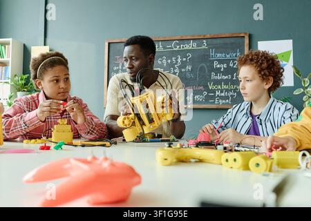 Black Male Teacher Guiding Children Building Robots in Stem Class Stock Photo