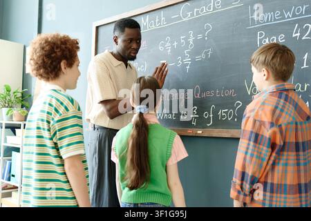 Black Male Teacher Explaining Math Problem to School Children Stock Photo