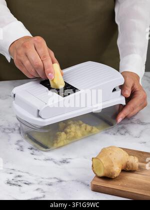Woman grating fresh ginger on manual vegetable slicer with grater attachment on marble table closeup Stock Photo