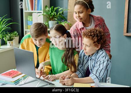 Diverse Teenagers Collaborating on Laptop during Classroom Project Stock Photo