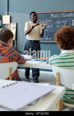 Black Male Teacher Explaining Math Lesson to Students in Classroom Stock Photo