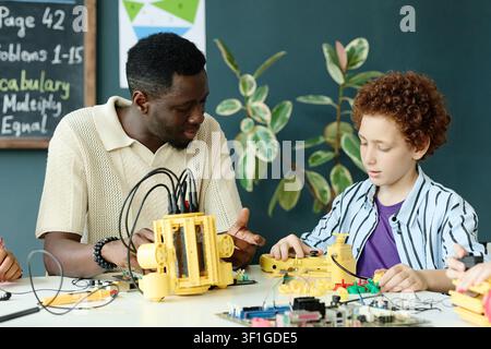 Black Male Teacher Guiding Schoolboy in Robotics Stem Lesson Stock Photo
