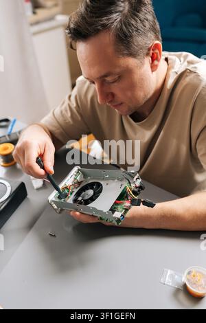 Vertical portrait of technician male working on electronic device, holding computer hardware with exposed cooling fan, performing repairs and Stock Photo