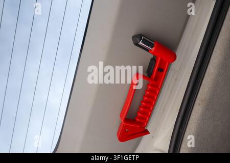 A red emergency escape tool mounted inside vehicle rear hatch, bright red plastic handle with seatbelt cutter and window breaker, safety device for ro Stock Photo
