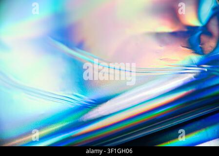 Close-up holographic surface with rippled texture displaying vibrant blue, pink, and yellow light reflections. Material shows metallic sheen and abstr Stock Photo