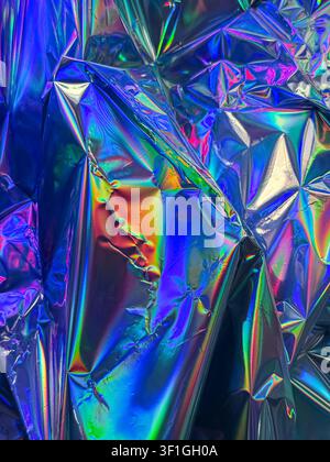 Highly reflective wrinkled holographic foil displaying vibrant spectrum of colors and strong light reflections. Abstract background with shiny surface Stock Photo