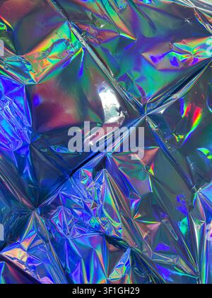 Crinkled iridescent foil surface reflecting vibrant blue, green and purple light. Textured abstract background with a glossy, metallic sheen, suggesti Stock Photo