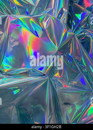 Crinkled holographic foil reflects vibrant rainbow colors and metallic sheen. Close up studio shot of textured surface with sharp folds and geometric Stock Photo