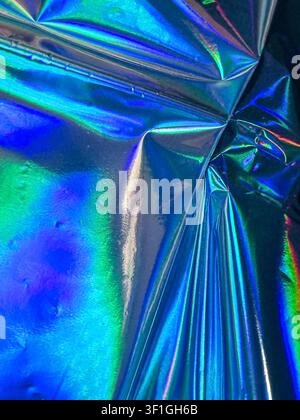 Close up of iridescent crumpled foil reflecting blue and green light. Shiny, reflective surface demonstrates metallic texture. Ideal for abstract back Stock Photo