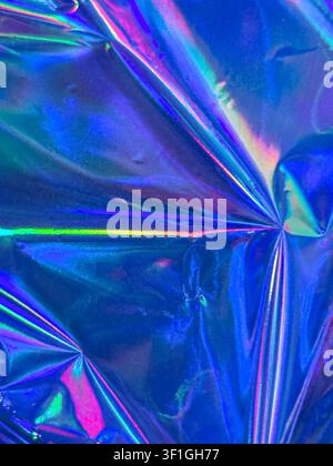 Crinkled holographic blue foil surface with iridescent rainbow highlights. Reflective texture creates abstract light patterns, ideal for futuristic an Stock Photo