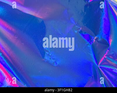Close up of crumpled holographic foil with vibrant blue and pink gradient reflections. Textured surface displays dramatic light play and smooth irides Stock Photo