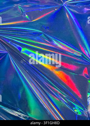 Close up textured iridescent foil surface reflecting rainbow spectrum of colors. Shiny crumpled material with light flares and dramatic shadows, perfe Stock Photo