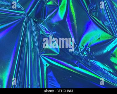 Iridescent crumpled foil surface reflecting blue and green hues. Clean, geometric patterns created by light and shadow. Suitable for futuristic, abstr Stock Photo