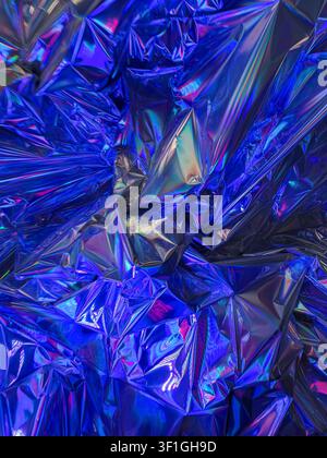 Close up textured surface of crinkled holographic material showing vibrant blue and magenta highlights. Reflective glossy folds create abstract patter Stock Photo