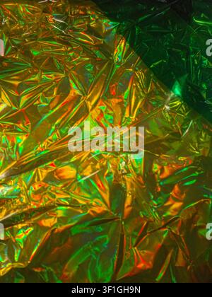 Bright yellow gold and green holographic foil crumpled texture. Reflective iridescent surface with sharp highlights and shadows. Dynamic abstract back Stock Photo