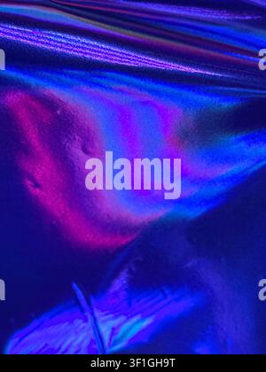 Metallic material surface reflects vibrant iridescent colors including pink, purple, and blue. Smooth lighting accentuates textured folds and highligh Stock Photo