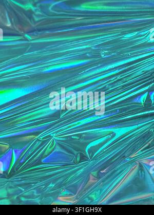 Abstract shimmering surface with iridescent teal and blue hues. Wrinkled metallic texture reflects light creating vibrant colorful patterns. Minimalis Stock Photo