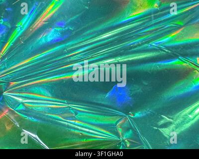 Close up of crumpled shiny metallic green foil with iridescent rainbow light reflections. Abstract textured background with vibrant colors and dynamic Stock Photo