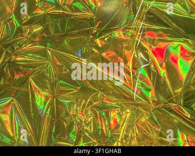 Intricate crinkled texture of gold metallic foil reflecting vibrant iridescent colors. Close up studio shot highlighting shiny surface and sharp geome Stock Photo