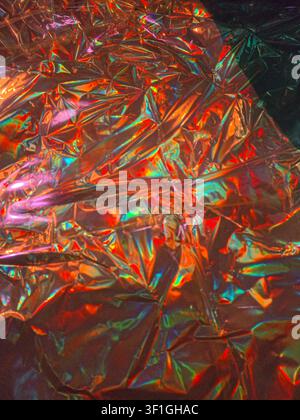 Crumpled iridescent metallic foil surface reflecting vibrant spectrum of colors like orange pink and green. Abstract background with dynamic light pla Stock Photo