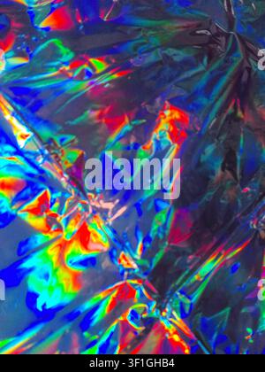 Metallic holographic foil crumpled texture reflects vibrant rainbow colors. Shiny, iridescent surface with abstract patterns, creating dynamic, futuri Stock Photo