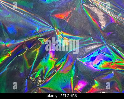 Abstract background texture featuring creased holographic foil reflecting vibrant iridescent colors and bright highlights. Metallic surface with shimm Stock Photo