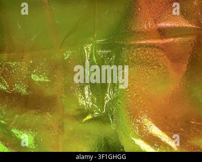 Close up of iridescent material surface texture with visible water droplets. Shimmering gradient transitions from vibrant yellow green to warm orange Stock Photo