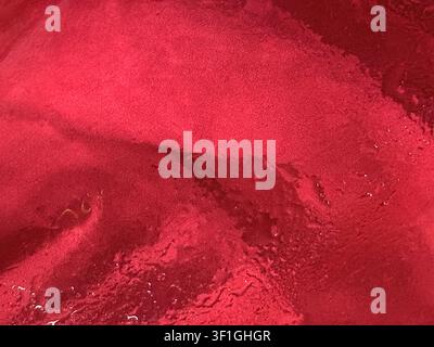 Close up view of a highly textured red surface with subtle water droplets scattered across. Reflective qualities with soft lighting accentuate varying Stock Photo
