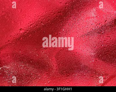 Close up of textured red fabric surface covered in small water droplets and condensation. Soft diffused lighting highlights the shiny liquid and matte Stock Photo