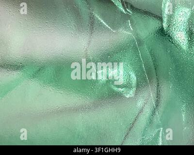 Subtle water droplets on a textured green translucent surface, creating abstract patterns. Soft diffused illumination highlights the fine granular det Stock Photo
