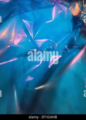 Abstract close up of iridescent blue plastic sheeting. Light reflects off crumpled surfaces creating bright pink and orange highlights over textured f Stock Photo