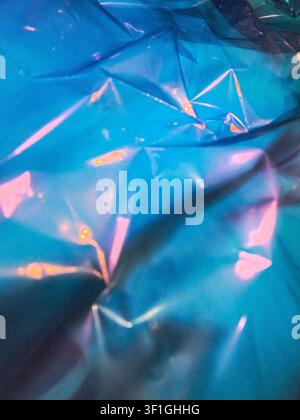 Iridescent blue plastic texture with soft pink highlights and subtle orange glows. Crumpled surface creates abstract patterns and shadows. Ideal for b Stock Photo