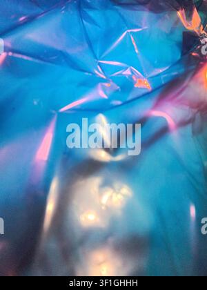 Abstract close up of crumpled iridescent blue plastic sheeting with pink and yellow highlights. Creates dynamic shimmering texture and highlights, sui Stock Photo