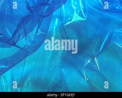 Abstract close up of crumpled blue plastic film layered over textured fabric creating shadows and highlights. Light diffusion effect. Stock Photo