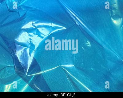Crinkled blue plastic material with reflective highlights and deep shadows creating abstract patterns. Subtle textile like texture visible under smoot Stock Photo