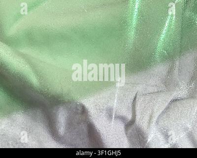 Close up abstract shot of textured fabric surface with smooth folds and subtle gradient from light green to silver. Reflective properties create shimm Stock Photo