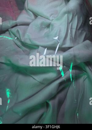 Textured fabric with dramatic folds and creases. Abstract bright green and pink light streaks illuminate surface, creating dynamic visual interest. Su Stock Photo
