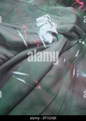 Green fabric textures and folds create abstract patterns under clear plastic sheeting. Reflective highlights and subtle red light add depth and visual Stock Photo