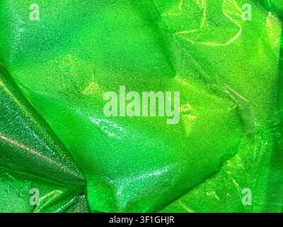 Abstract close up showing crumpled green plastic material with intricate water droplets reflecting light. Vibrant color gradient from dark to light gr Stock Photo