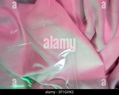 Macro detail of rumpled pink fabric under soft studio lights, showing texture and smooth folds. Plastic wrap creates subtle reflections, suggesting pa Stock Photo